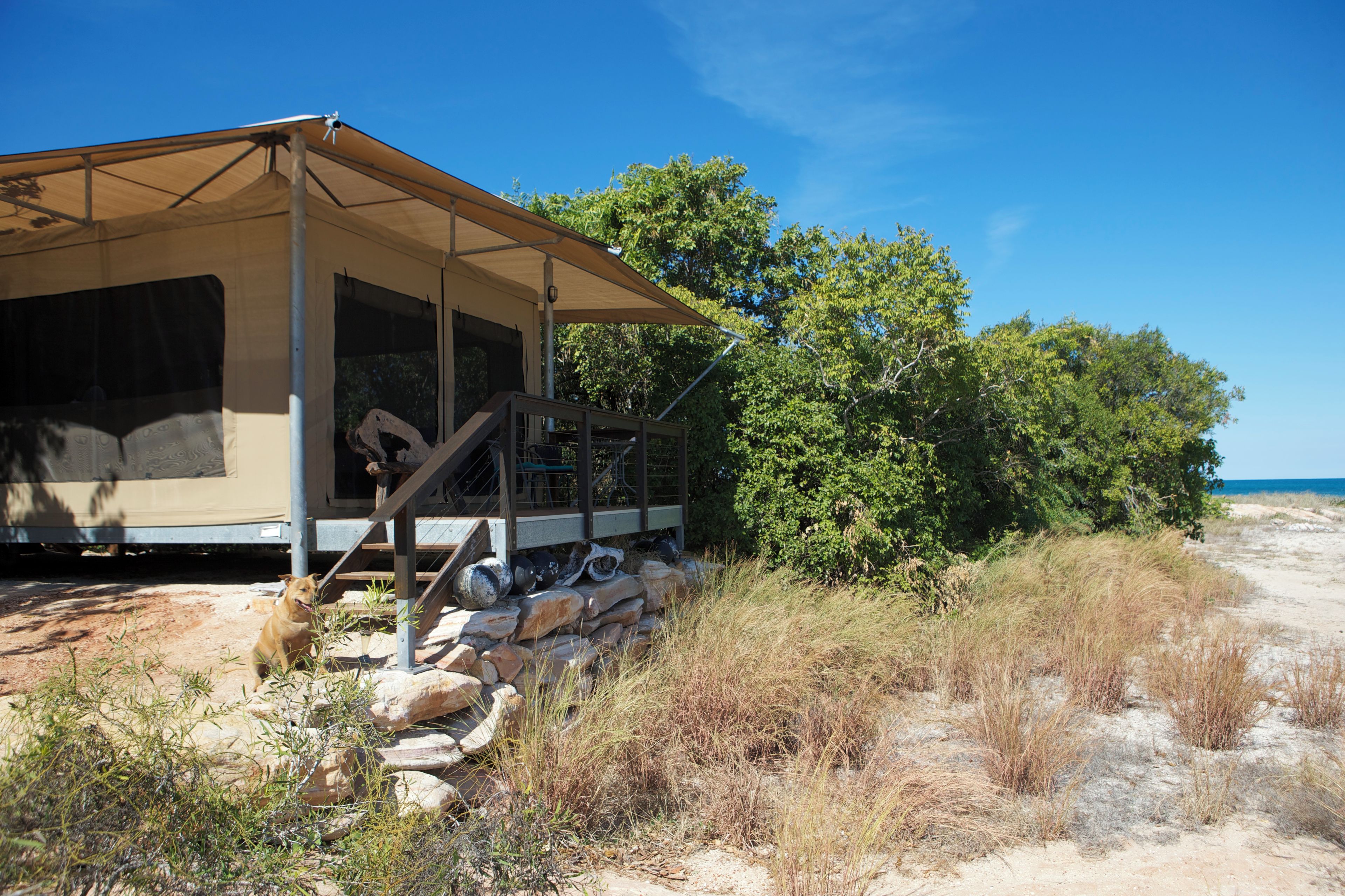 Una casetta sulla spiaggia con un portico coperto, una scala che conduce all'ingresso e vista sulla spiaggia e sull'oceano.