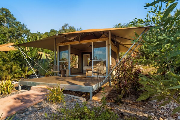 A modern outdoor structure with a covered patio, large windows, and a view of the surrounding greenery.