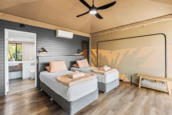 A bedroom with two beds, a ceiling fan, an air conditioning unit, and a small bedside table.