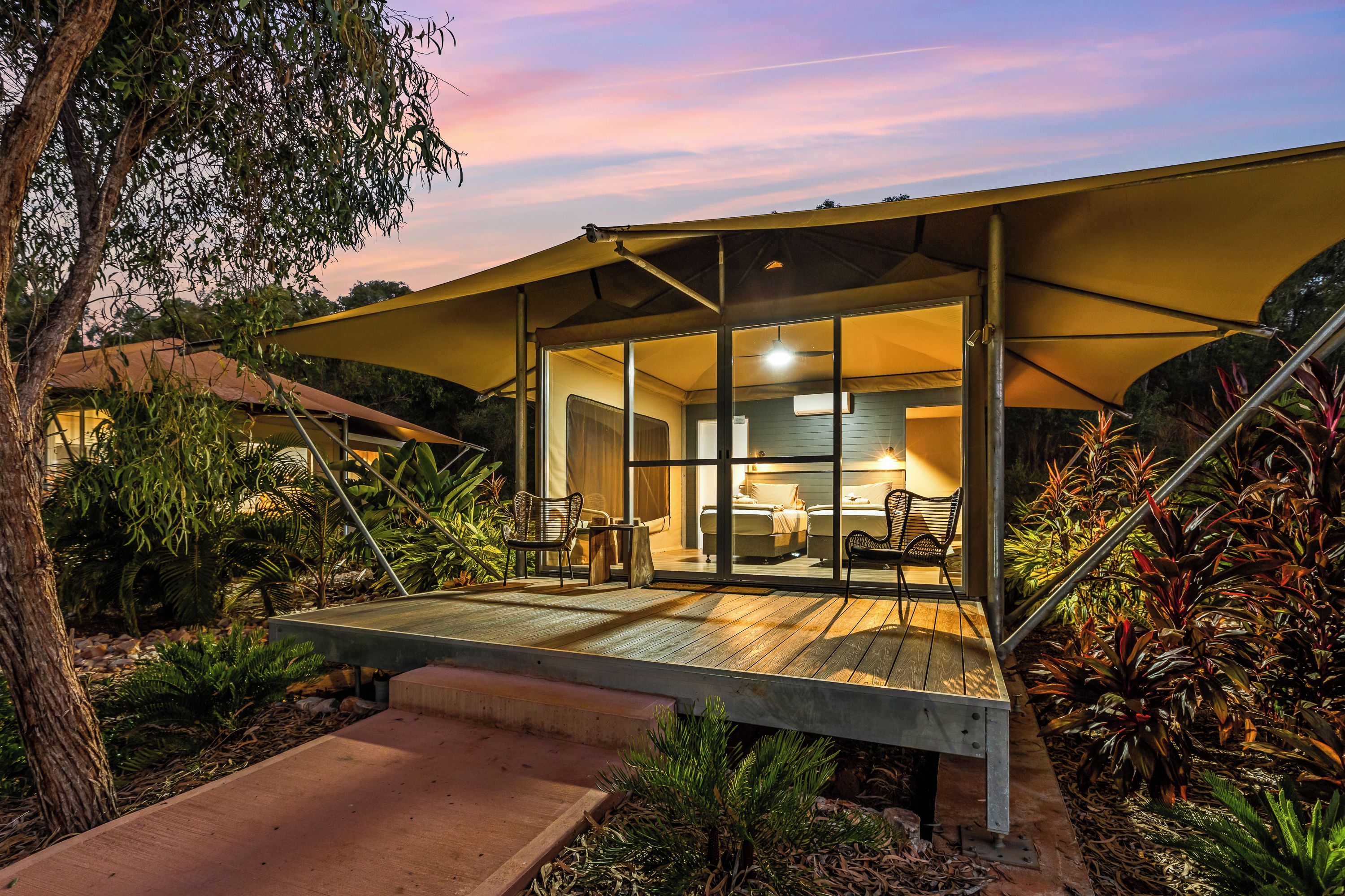 A modern outdoor lounge area with a wooden deck, glass walls, and a covered seating area.