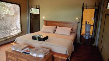 Una cama individual con cabecera de madera, una mesita de noche con un libro y una toalla, y una ventana con vistas a árboles.