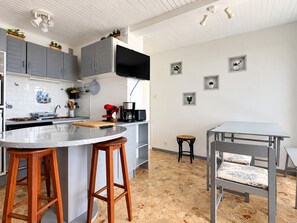 A modern kitchen with grey cabinets, a large island with stools, a dining table, and a small black stool. - Apartment panoramic view - 6 guests (Chamrousse)
