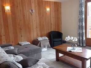 A room with a wooden wall, a sofa set, a black chair, a wooden table, and a window with curtains. - Family house, parking, pets - 6 guests (Valloire)