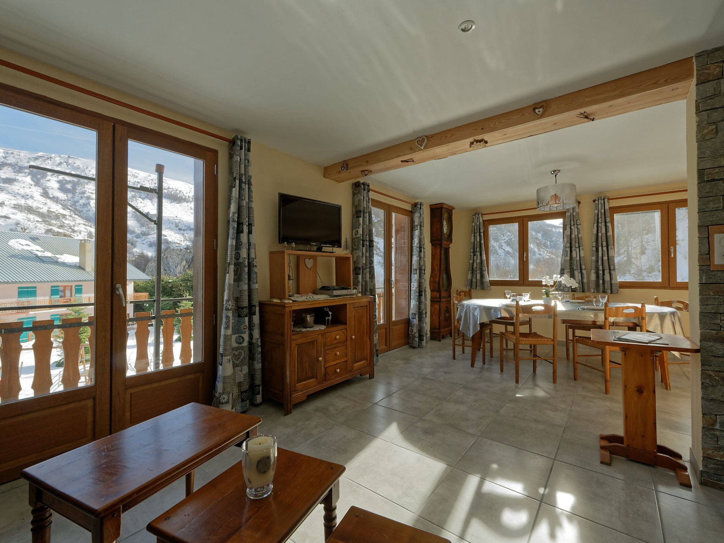 Ein geräumiges Zimmer mit Essbereich, Fernseher und Blick auf einen verschneiten Berg.