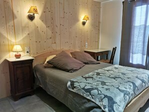 A bedroom with a wooden headboard, two bedside lamps, a bed with a patterned blanket, a nightstand, and a small table. - Family house, parking, pets - 6 guests (Valloire)