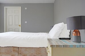 A neatly made bed with white linens, a bedside table with a lamp, and a remote control. - OYO The Billingford Horseshoes - Self Check IN (Diss)