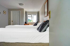 A hotel room with two beds, a window with curtains, a door, and a mirror on the wall. - OYO The Billingford Horseshoes - Self Check IN (Diss)