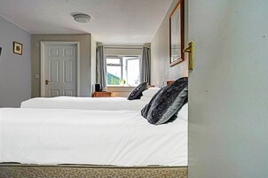 Una habitación de hotel con dos camas, una ventana con cortinas, una puerta y un espejo en la pared.