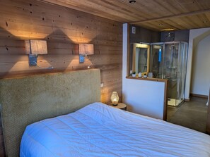A bedroom with a wooden ceiling, a bed with a white duvet, a bedside lamp, and a glass shower enclosure. - Apartment in Les Gets with private parking - 4 guests (Les Gets)