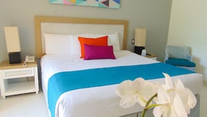 Ein ordentlich bezogenes Bett mit einer blau-weißen Tagesdecke, zwei Kissen in Orange und Violett sowie eine weiße Orchidee auf dem Bett.