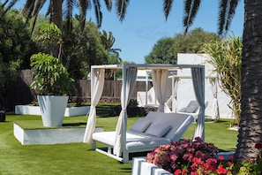 Un jardín con una cama con dosel blanco, una silla lounge blanca y una maceta grande con flores.