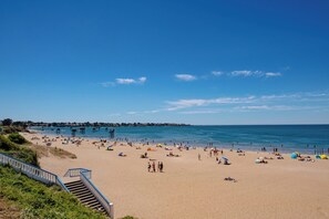 Ein Strand mit einer Treppe, die zum Sand führt, ein klarer Himmel und das Meer im Hintergrund.
