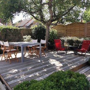 Eine Holzterrasse mit Tisch und Stühlen, umgeben von Grünpflanzen und einem Holzzaun.