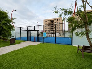 A fenced tennis court with a net, a bench, and a trash bin. - Nómada Living | 2 bedrooms, pool, and excellent location (Zaru)