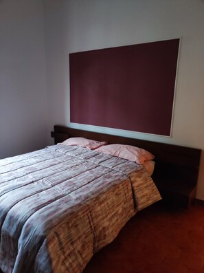 A bed with a patterned bedspread and pillows, a dark headboard, and a large, plain wall above. - MAISON PLATONE JOLIE (Alessandria)