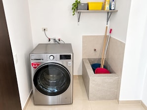 Ein kompakter, moderner Waschraum mit einer Waschmaschine mit Frontlader, einer kleinen Ablage für Reinigungsmittel und einem Mop-Halter.