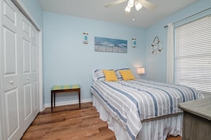 A bedroom with a bed, a nightstand, a bench, a ceiling fan, and a window with blinds. - Seaside at Anastasia B104 Condo (St. Augustine)