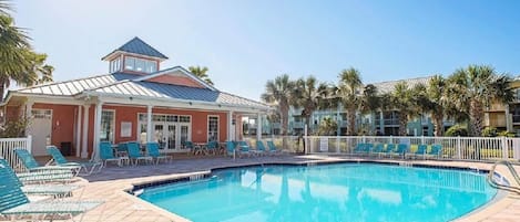 Une piscine avec des chaises longues et un bâtiment à la façade rouge et au toit bleu.