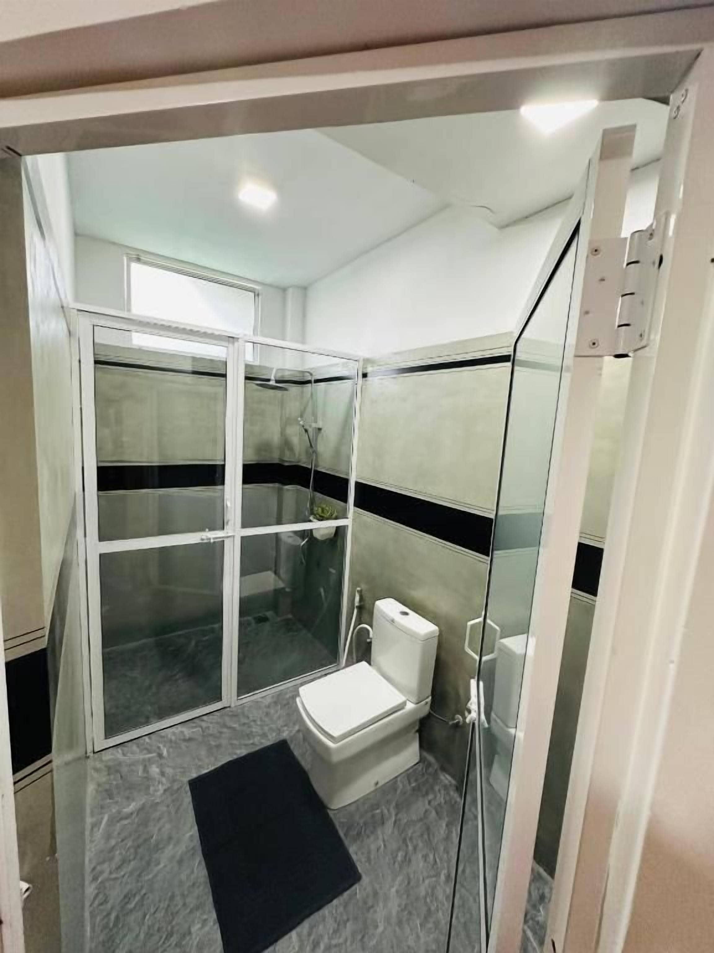 Un baño moderno con cabina de ducha de vidrio, inodoro y alfombra de baño negra.