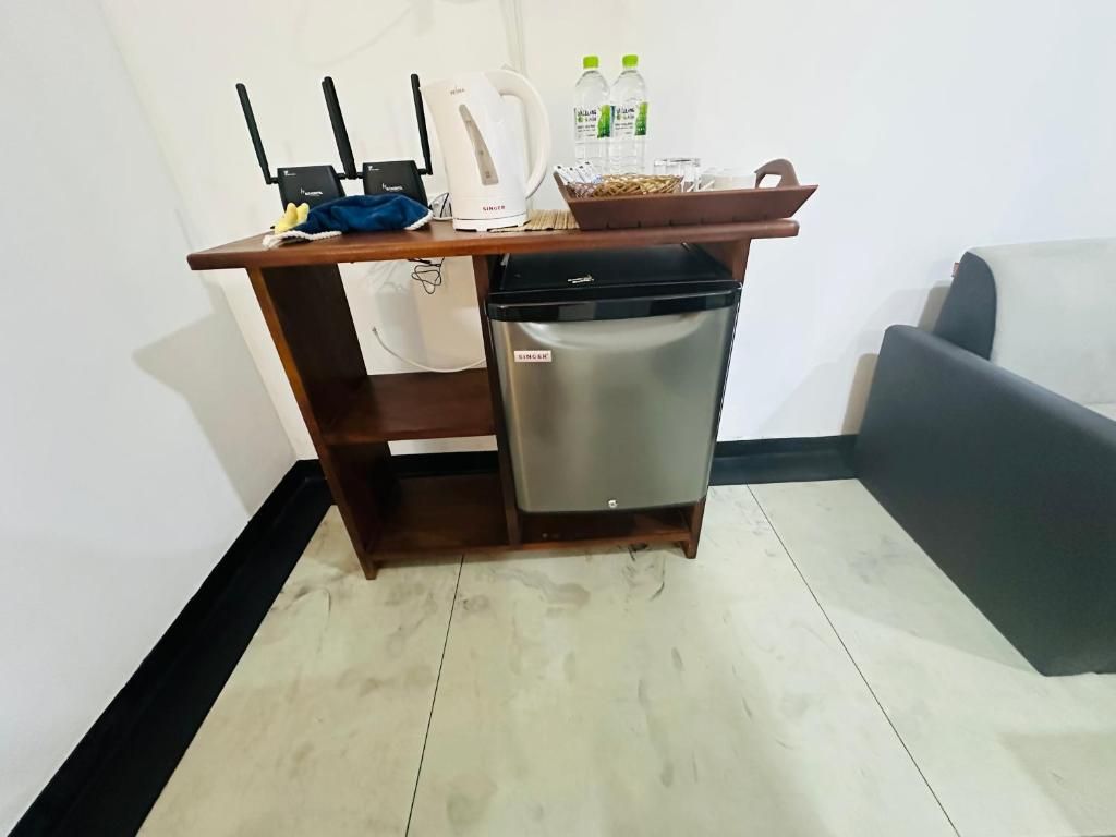 A compact kitchenette with a refrigerator, a kettle, and a coffee maker. There are two bottles of water and a basket on the counter.