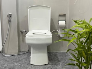 A bathroom with a white toilet, a shower, and a roll of toilet paper dispenser. - Peak Blooms (Ella)