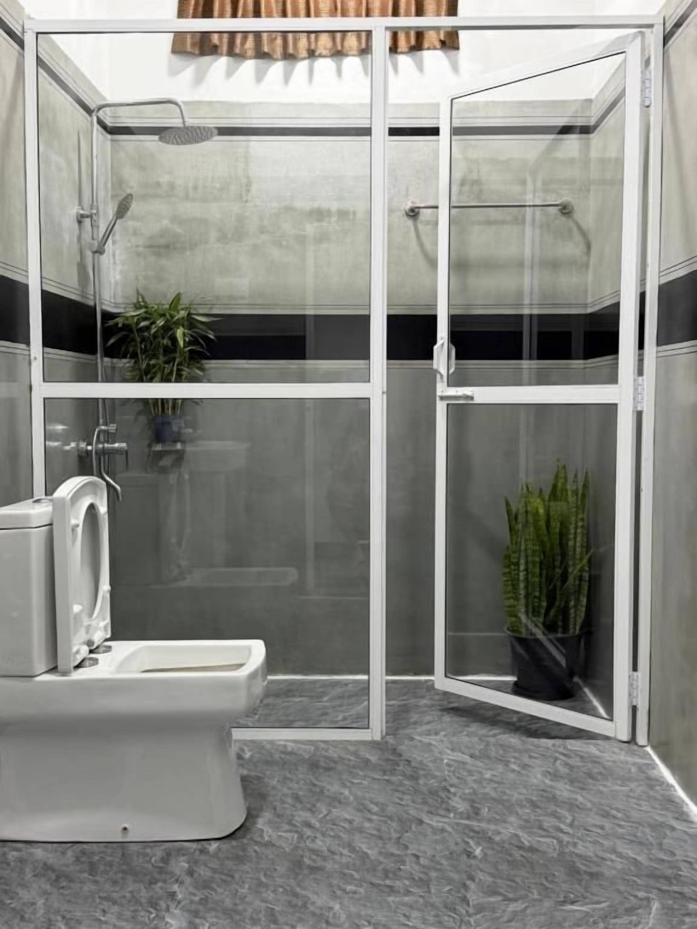 Un baño moderno con ducha envuelta en cristal, inodoro y dos plantas en macetas.