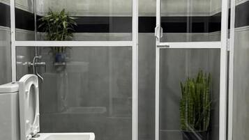 Un baño moderno con ducha envuelta en cristal, inodoro y dos plantas en macetas.