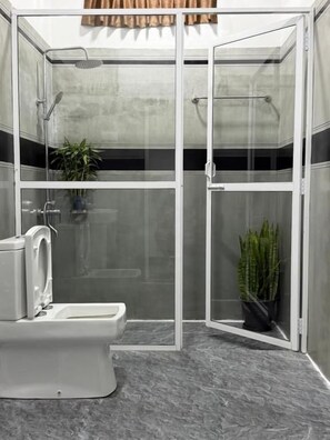 A modern bathroom with a glass-enclosed shower, a toilet, and two potted plants. - Peak Blooms (Ella)