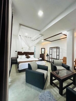 Una habitación de hotel con una cama, dos sofás, una mesita de centro y una mesita de noche.