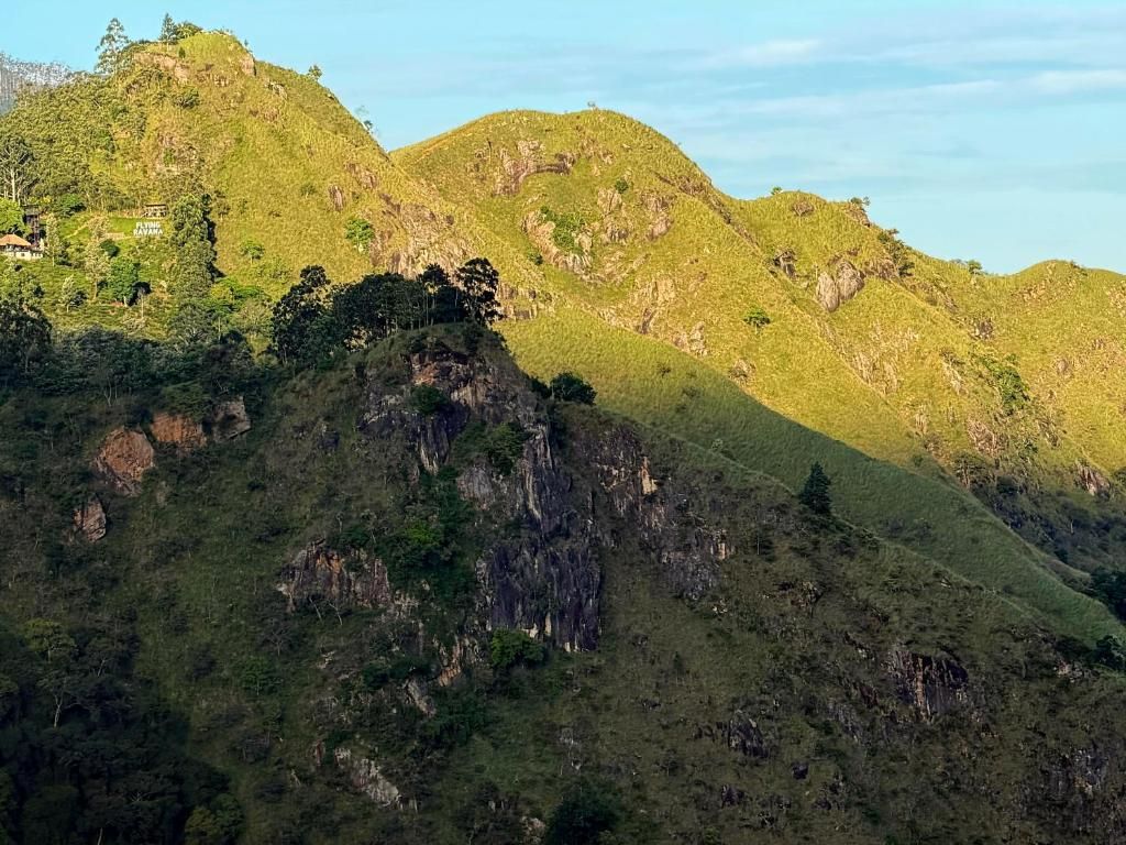 Eine Berglandschaft mit einer markanten Felsformation im Vordergrund und einem Gebäude auf einem Hügel im Hintergrund.