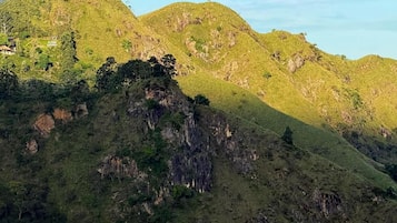 Eine Berglandschaft mit einer markanten Felsformation im Vordergrund und einem Gebäude auf einem Hügel im Hintergrund.