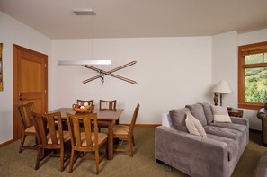 A dining area with wooden chairs and a table, a gray sofa, and a window with a view of greenery. - Luxury One Bedroom, Capitol Peak, Base Village steps away from lifts. (Snowmass Village)