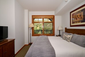 Een slaapkamer met een groot bed, een televisie op een houten dressoir, twee bedlampen en een raam met uitzicht op groen.