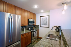A modern kitchen with stainless steel appliances, wooden cabinets, a granite countertop, and a built-in oven. - Luxury One Bedroom, Capitol Peak, Base Village steps away from lifts. (Snowmass Village)