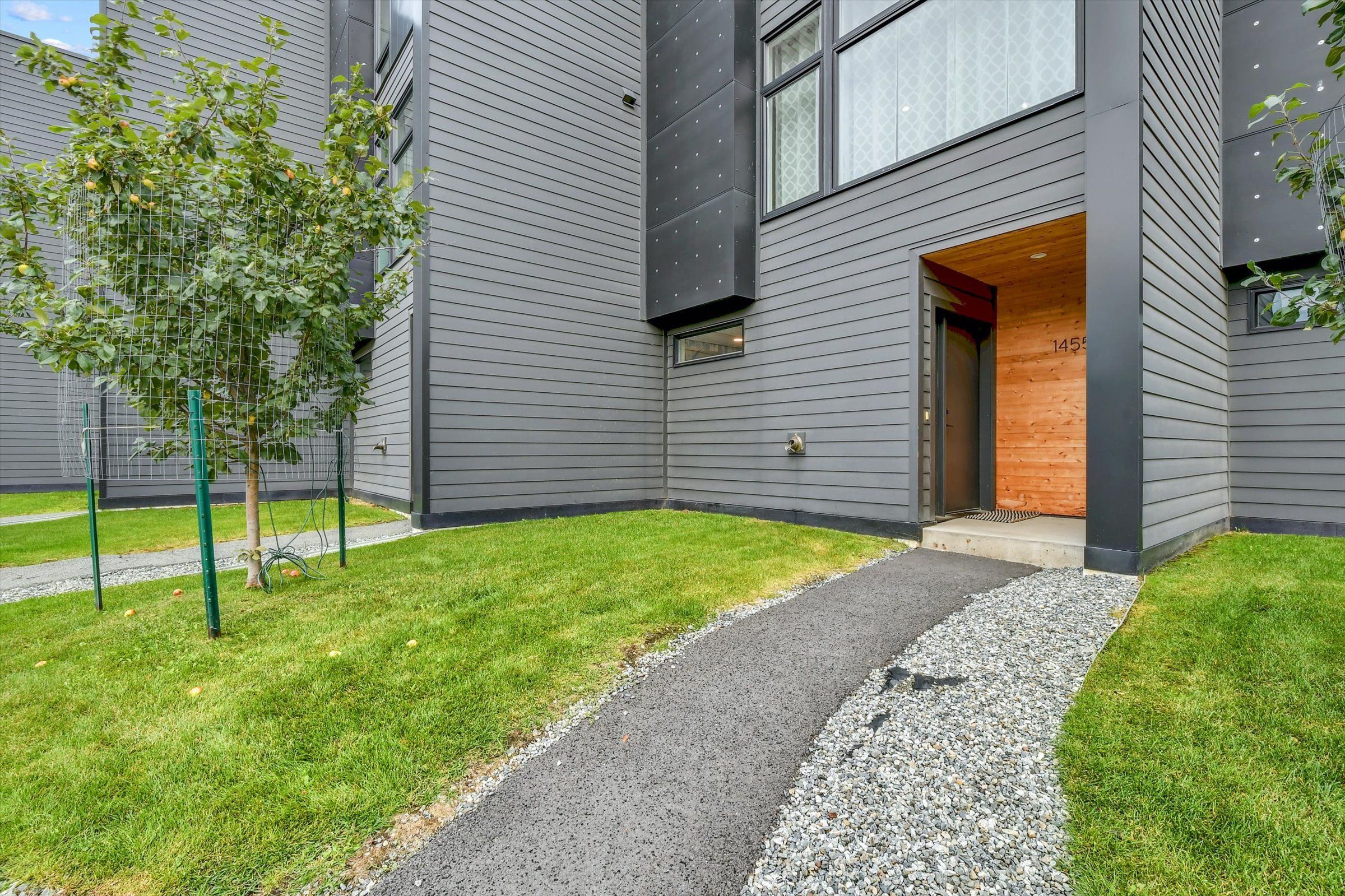 A modern building with a grey exterior, a wooden door, and a small tree in the foreground.