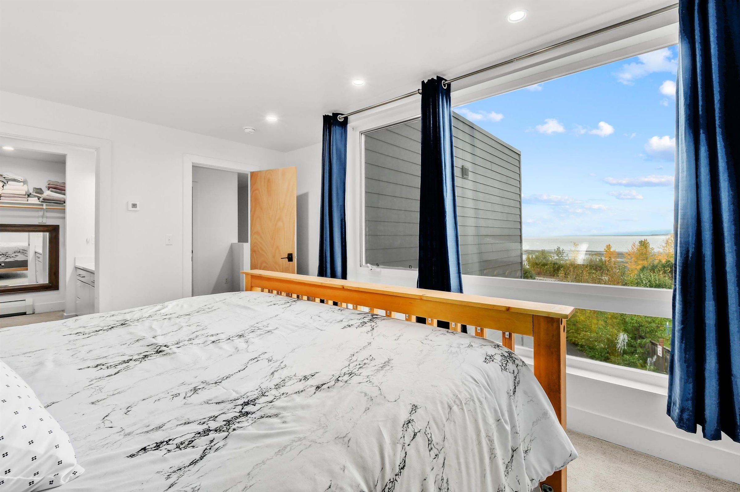 A bright bedroom with a wooden bed frame, large picture window, and scenic view.