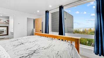 A bright bedroom with a wooden bed frame, large picture window, and scenic view.