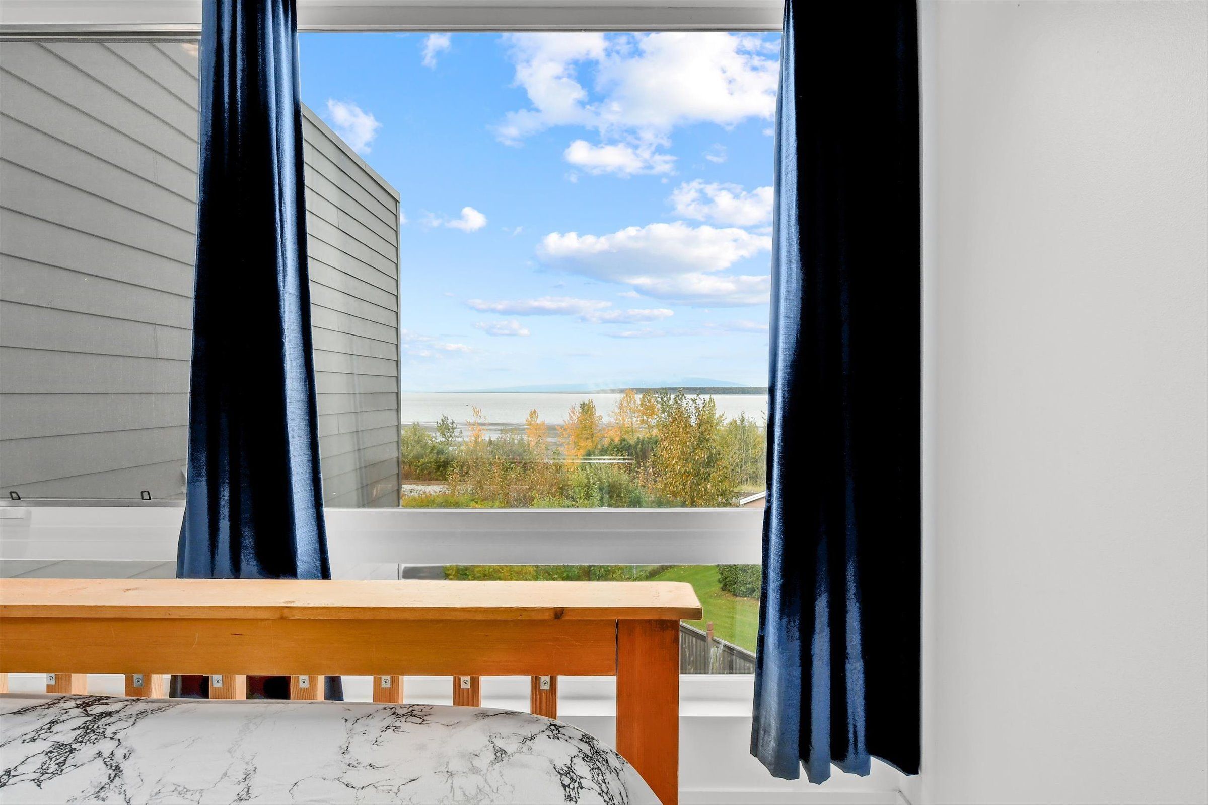 Bedroom window framed by blue curtains with views of distant water and trees.