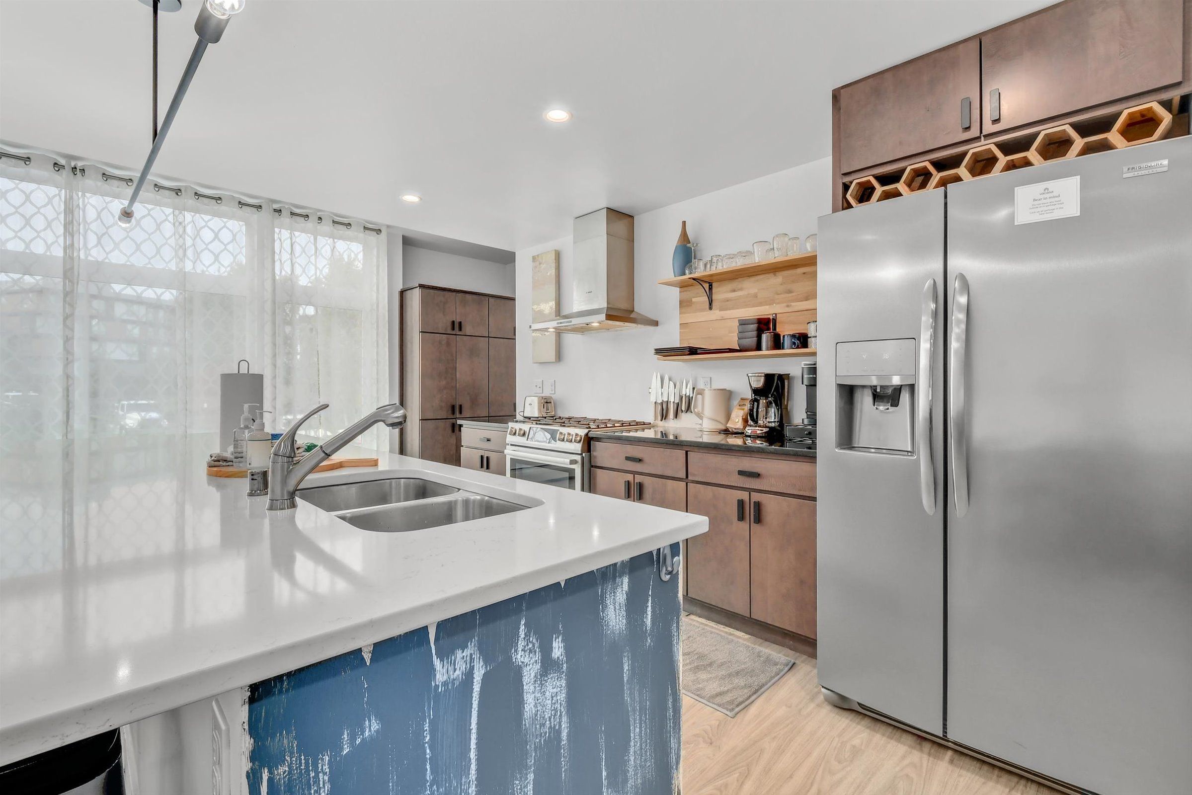 Kitchen with a central sink island, stainless steel refrigerator, and wood cabinetry.