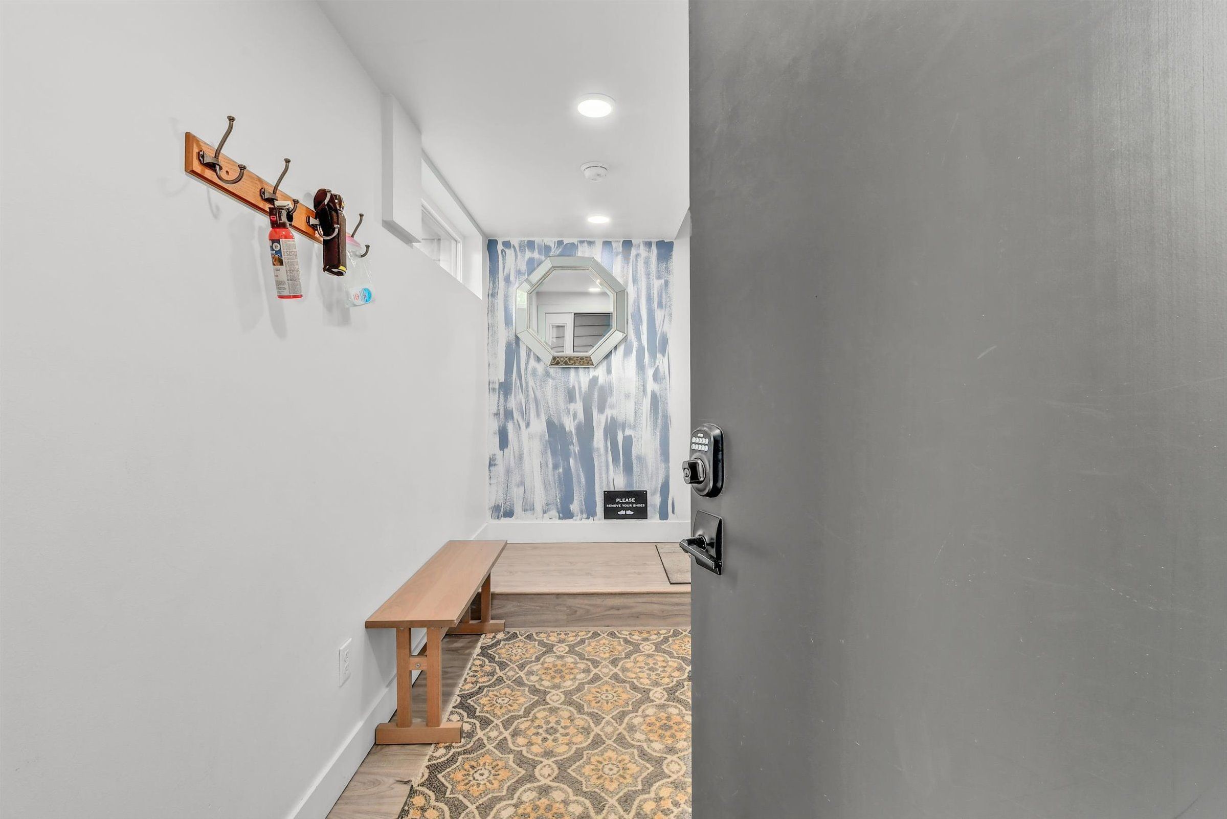 An entryway features a wood bench, patterned runner rug, and blue accent wall.