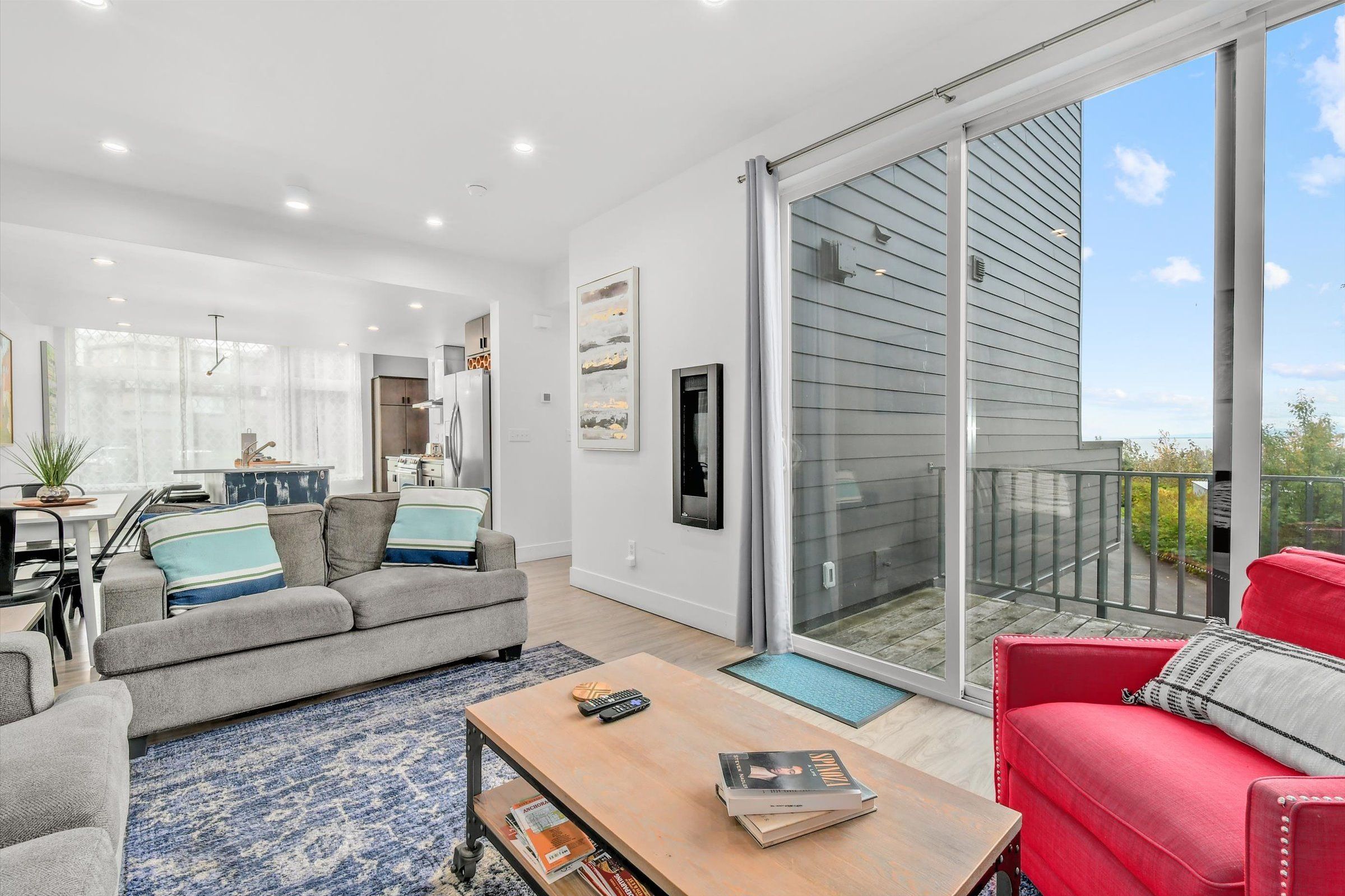 Bright living room with seating, a sliding glass door to a deck, and an open layout to the kitchen.