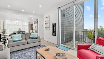 Bright living room with seating, a sliding glass door to a deck, and an open layout to the kitchen.
