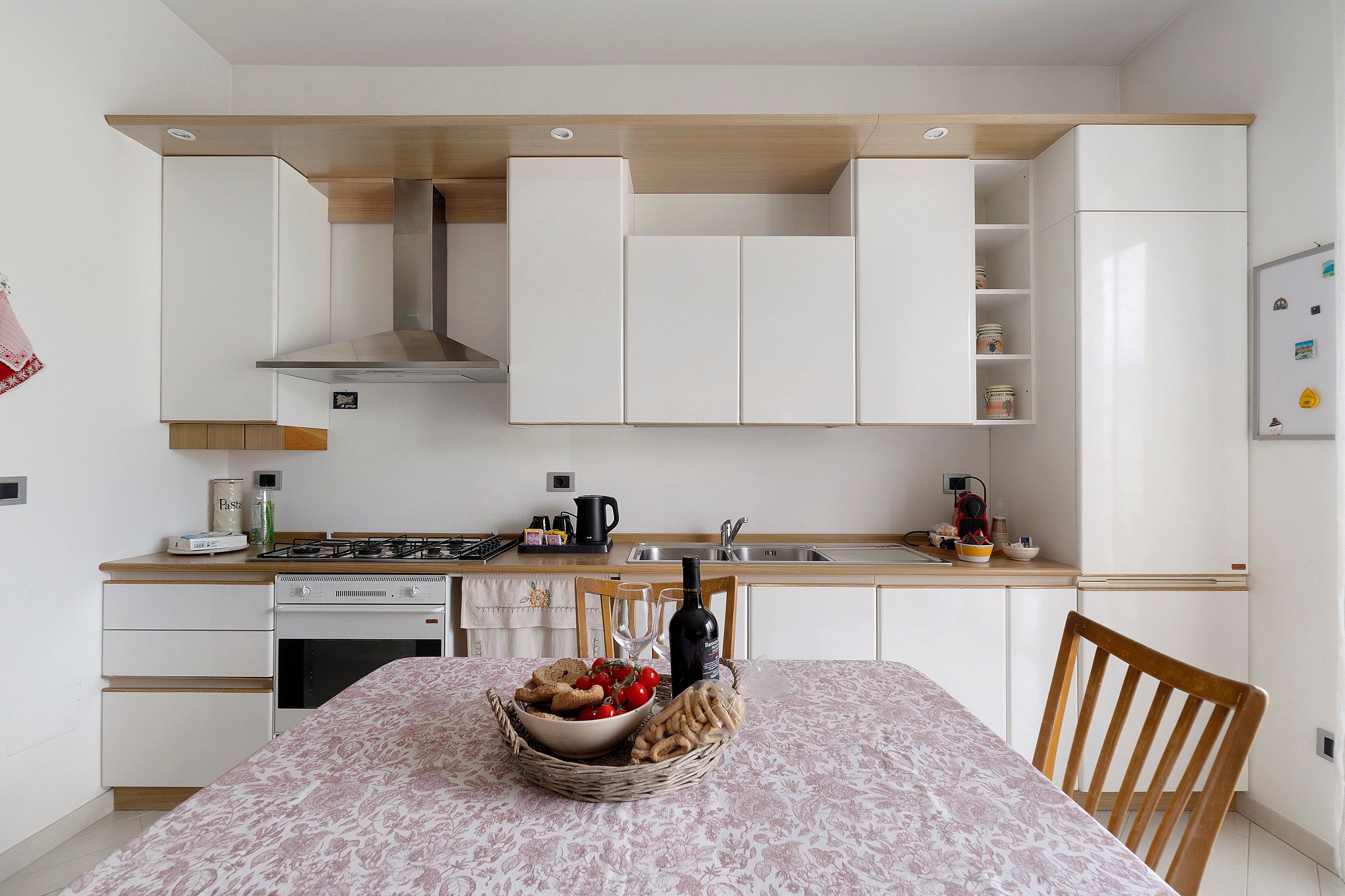 A compact kitchen with white cabinets, a stove, and a dining table set with a basket of bread and tomatoes.