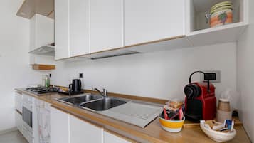 Une cuisine moderne avec des meubles blancs, un évier en acier inoxydable, une cuisinière à gaz et une machine à café rouge.