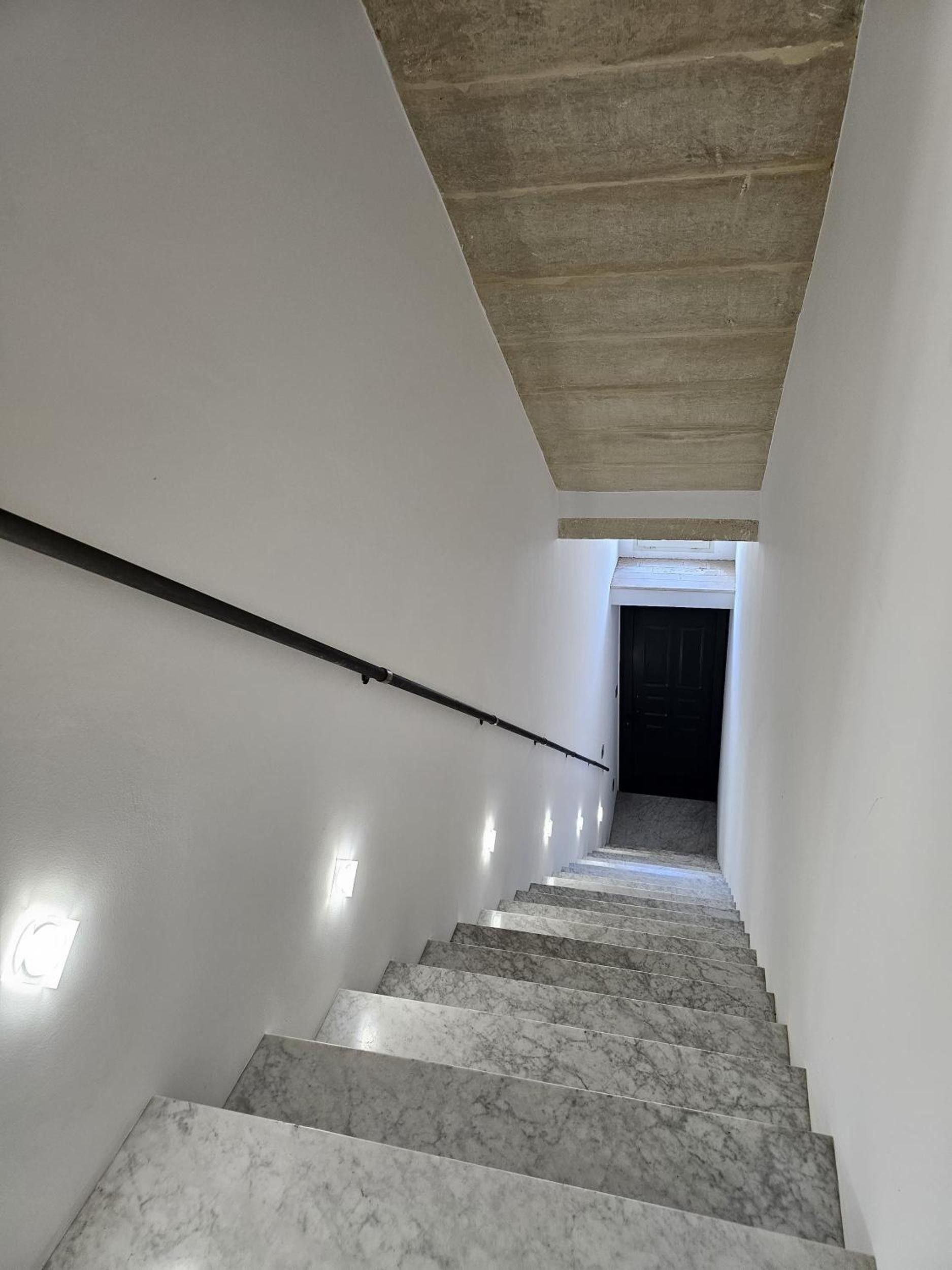 Un escalier muni d’une rampe, menant à une porte sombre située en haut.