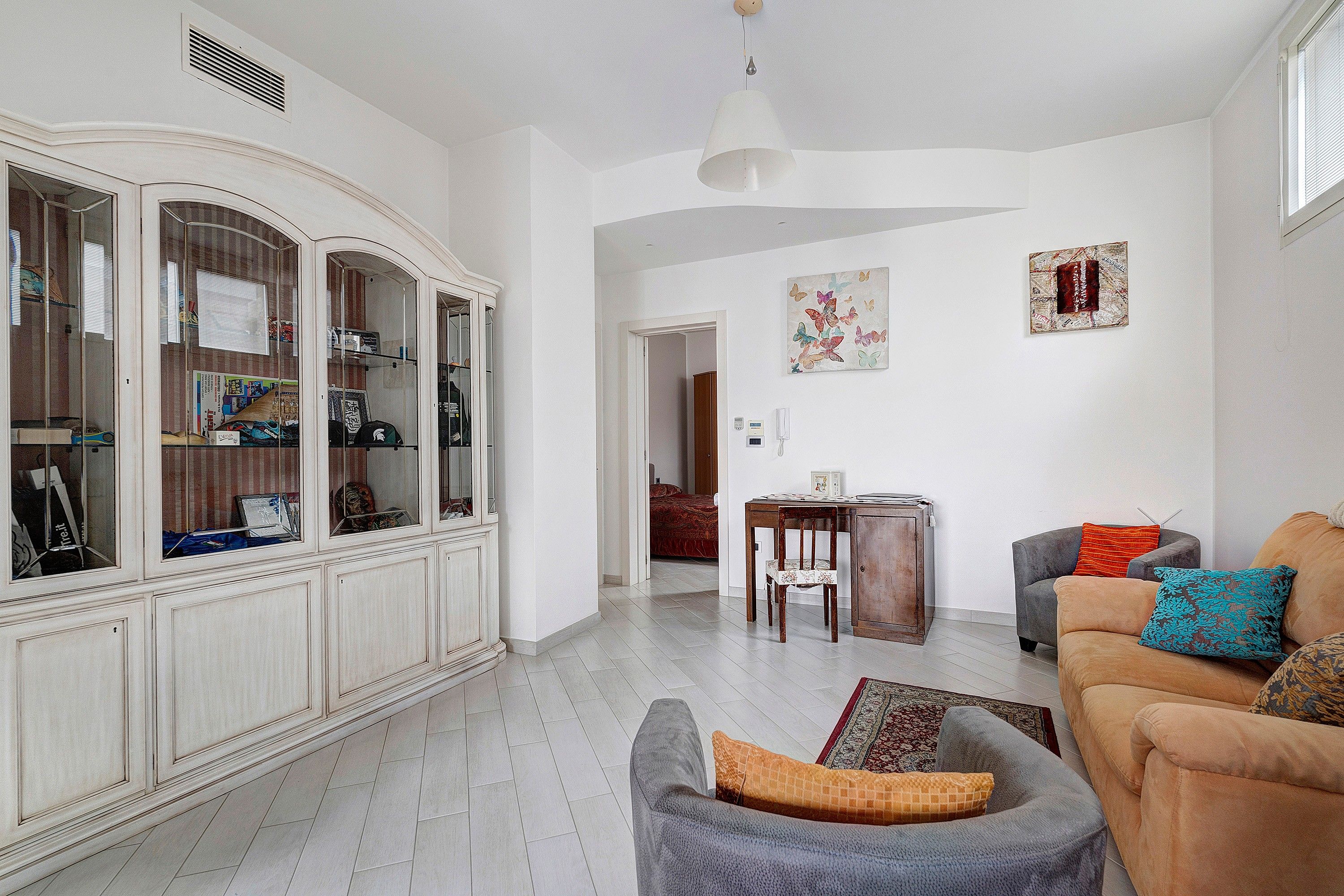 Un salon spacieux avec un meuble blanc, un fauteuil gris, un canapé marron et un coin repas comprenant une table et des chaises en bois.