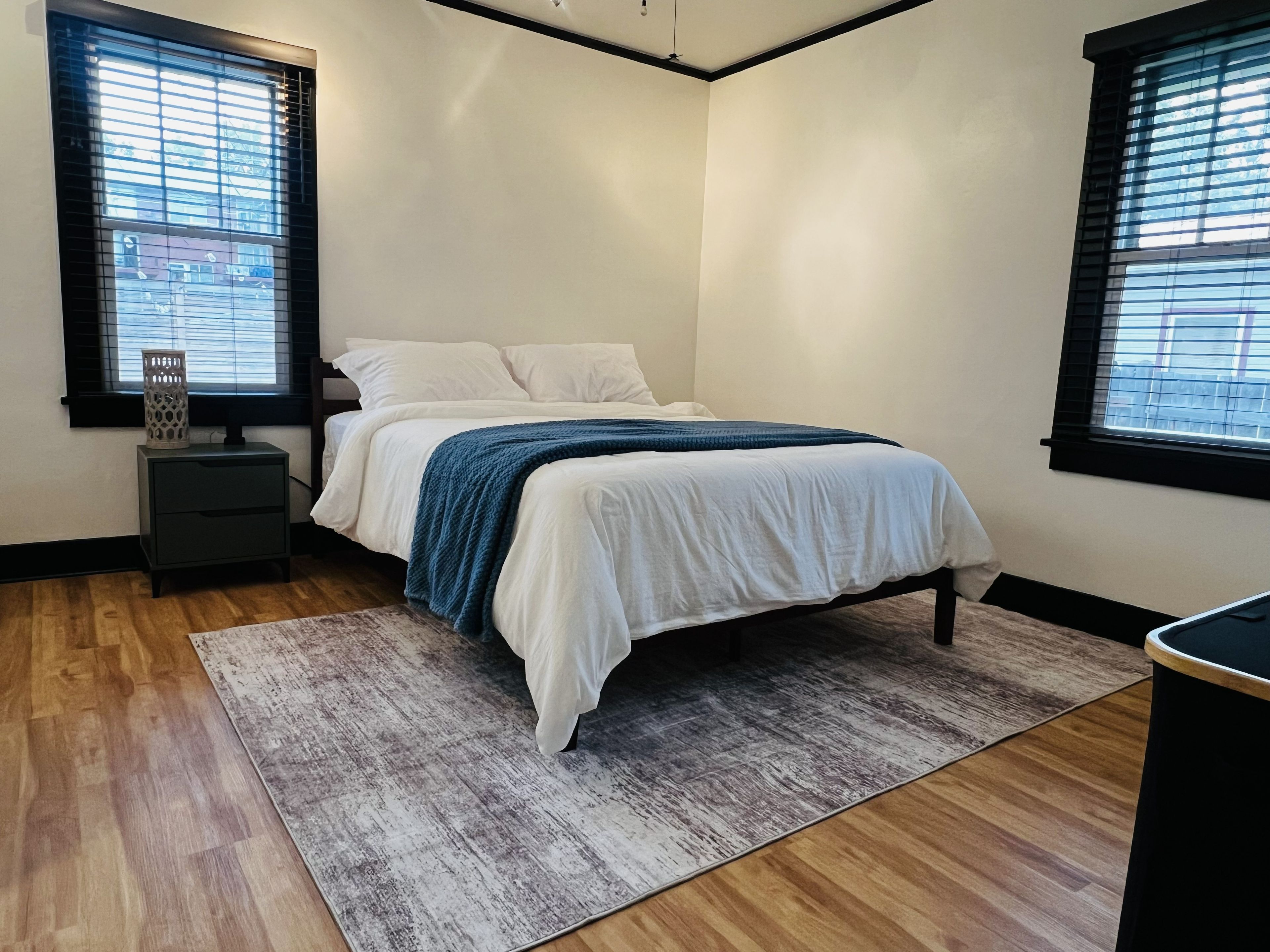 Un dormitorio con cama, mesitas de noche, alfombra y ventanas.