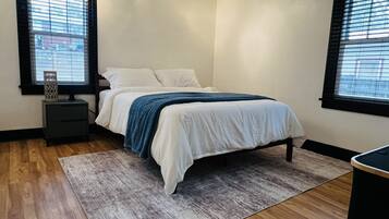 Un dormitorio con cama, mesitas de noche, alfombra y ventanas.
