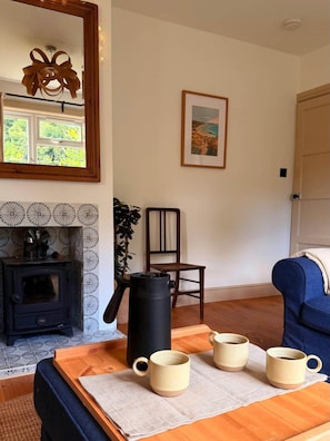 A cozy living room with a fireplace, a coffee table with mugs, a chair, and a framed picture on the wall. - Groom's Cottage, Jedburgh (Jedburgh)