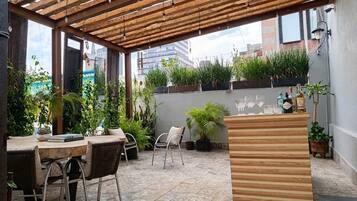 Un patio exterior con una pérgola de madera, una mesa de comedor con sillas y plantas en macetas.